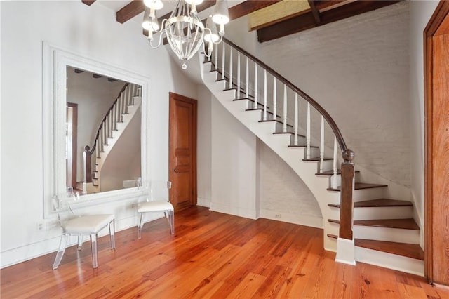 stairway featuring hardwood / wood-style flooring, beamed ceiling, and an inviting chandelier