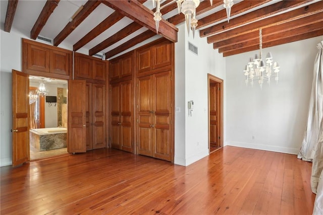 unfurnished living room featuring beam ceiling, light wood-type flooring, and a notable chandelier