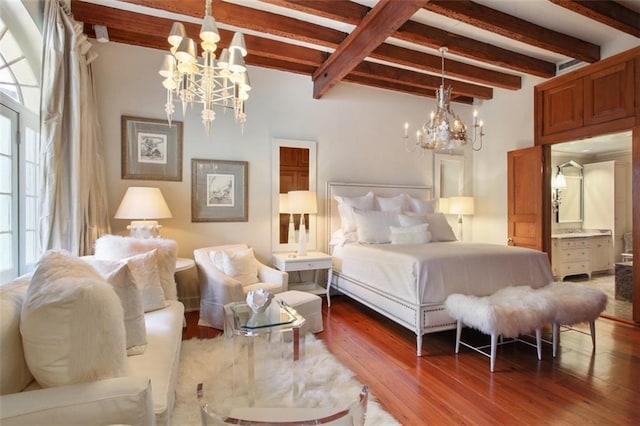 bedroom with beamed ceiling, hardwood / wood-style flooring, an inviting chandelier, and ensuite bath