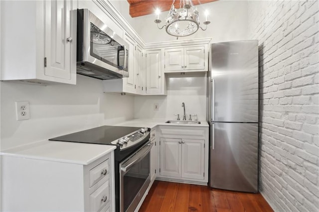 kitchen with sink, white cabinets, brick wall, and appliances with stainless steel finishes