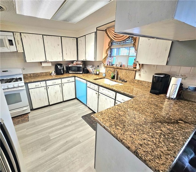 kitchen with sink, light hardwood / wood-style flooring, dark stone countertops, appliances with stainless steel finishes, and kitchen peninsula