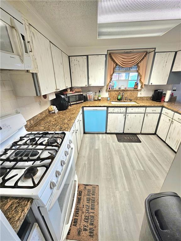 kitchen with sink, a textured ceiling, dark stone countertops, light wood-type flooring, and white appliances