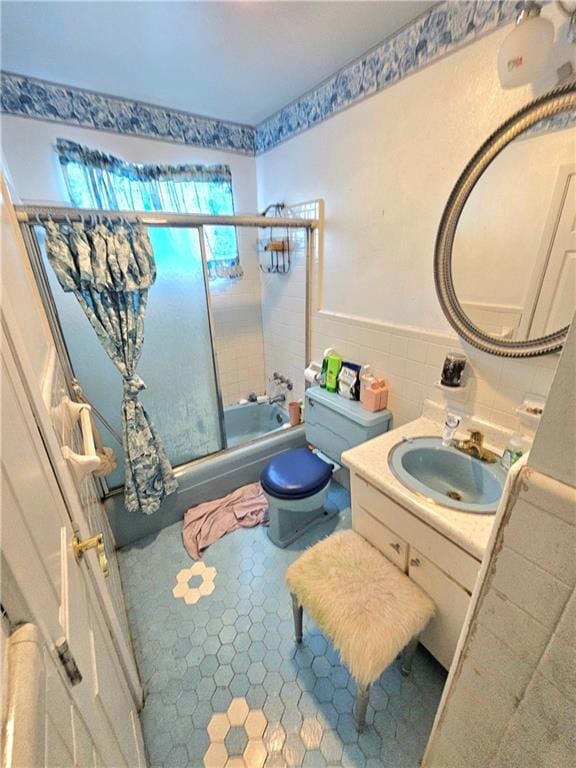 full bathroom with tile walls, vanity, toilet, and combined bath / shower with glass door