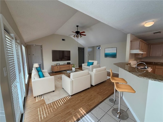 living room with vaulted ceiling, ceiling fan, light tile patterned floors, and a textured ceiling