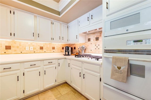 kitchen with light tile patterned floors, white appliances, crown molding, white cabinetry, and backsplash