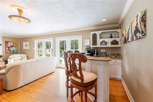 bar featuring white cabinets, ornamental molding, a textured ceiling, and light wood-type flooring