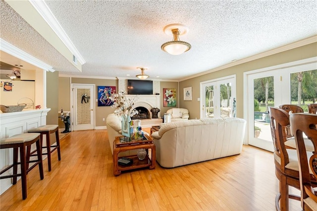 living room with light hardwood / wood-style flooring, ornamental molding, a large fireplace, a textured ceiling, and french doors