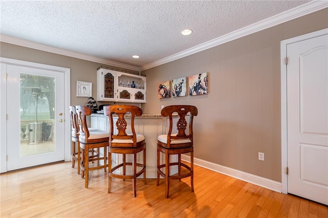 interior space with indoor bar, ornamental molding, light hardwood / wood-style flooring, and a textured ceiling