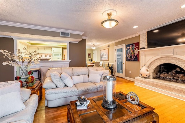 living room featuring crown molding, a fireplace, a textured ceiling, and light wood-type flooring