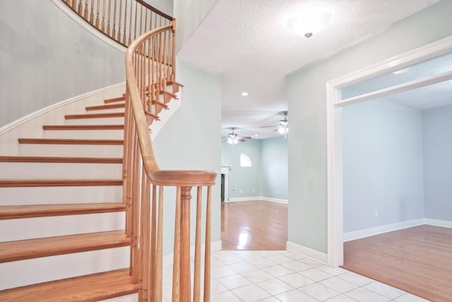 stairway with tile patterned flooring, ceiling fan, and a textured ceiling