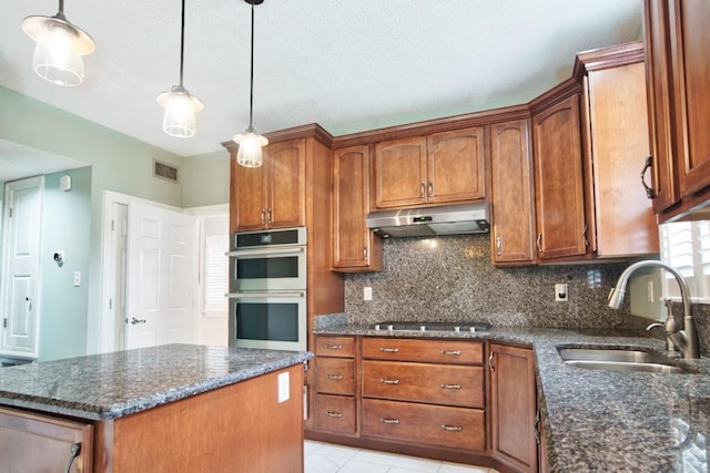 kitchen featuring sink, dark stone counters, double oven, and decorative light fixtures