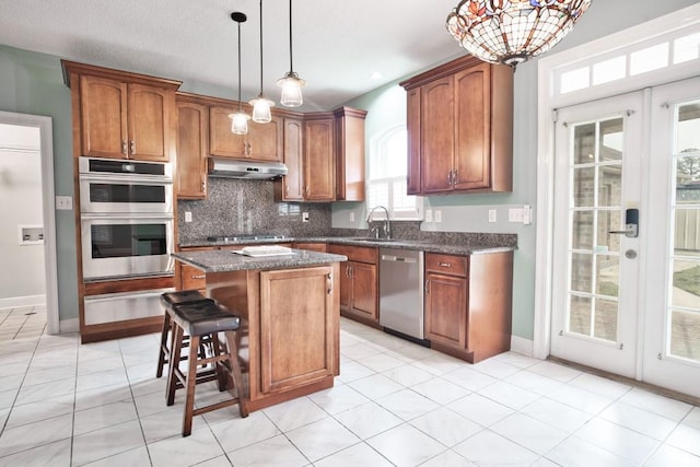 kitchen with appliances with stainless steel finishes, a breakfast bar, sink, hanging light fixtures, and a center island