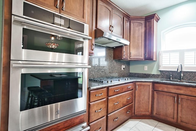 kitchen with sink, light tile patterned floors, dark stone countertops, stainless steel appliances, and decorative backsplash