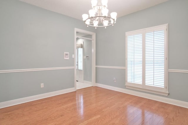 spare room with an inviting chandelier, light hardwood / wood-style floors, and a wealth of natural light