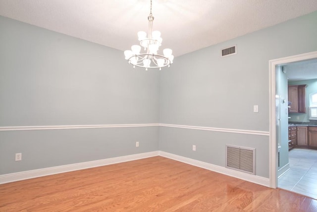 spare room with a notable chandelier and light hardwood / wood-style floors