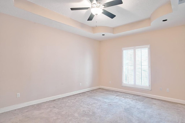 carpeted spare room with ceiling fan and a tray ceiling