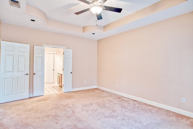 unfurnished bedroom featuring ceiling fan, a raised ceiling, and light carpet