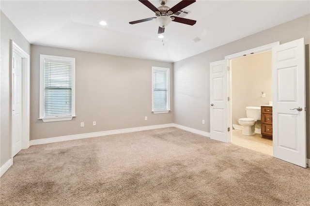 unfurnished bedroom with a raised ceiling, ceiling fan, light colored carpet, and connected bathroom