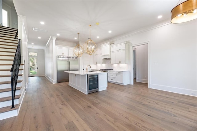 kitchen featuring a center island with sink, hanging light fixtures, wine cooler, white cabinetry, and stainless steel appliances