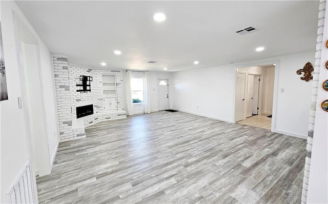 unfurnished living room featuring light hardwood / wood-style flooring and a brick fireplace