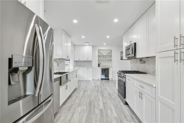 kitchen with backsplash, stainless steel appliances, sink, white cabinetry, and wine cooler