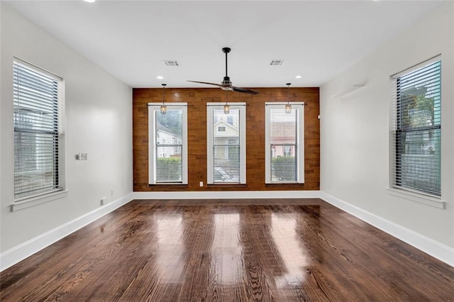 unfurnished room with ceiling fan with notable chandelier, a wealth of natural light, and wooden walls