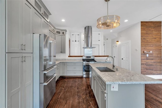 kitchen with wall chimney range hood, sink, hanging light fixtures, light stone countertops, and stainless steel appliances