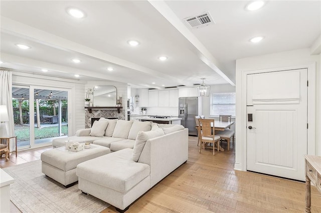 living room with a fireplace, beam ceiling, light hardwood / wood-style floors, and a chandelier