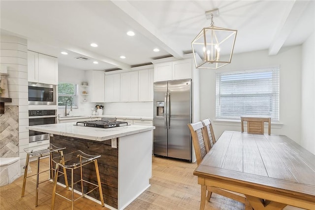 kitchen featuring appliances with stainless steel finishes, sink, decorative light fixtures, beamed ceiling, and a kitchen island