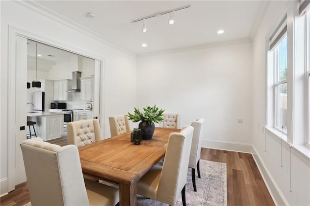 dining space with dark hardwood / wood-style flooring, track lighting, and ornamental molding