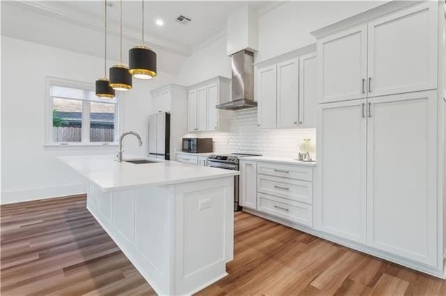 kitchen with sink, wall chimney range hood, decorative light fixtures, a kitchen island with sink, and stainless steel range with electric cooktop