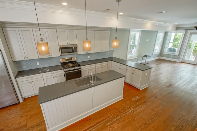 kitchen featuring pendant lighting, sink, kitchen peninsula, stainless steel appliances, and light hardwood / wood-style flooring