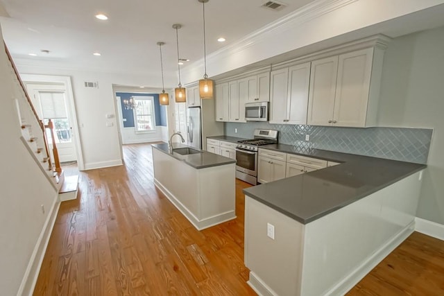 kitchen with sink, appliances with stainless steel finishes, decorative light fixtures, kitchen peninsula, and light wood-type flooring