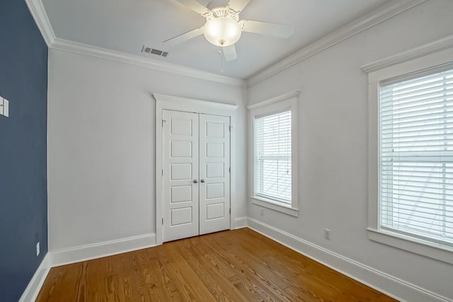 unfurnished bedroom with hardwood / wood-style floors, crown molding, a closet, and ceiling fan