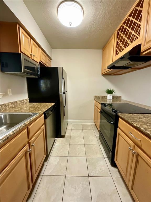 kitchen with sink, a textured ceiling, range hood, appliances with stainless steel finishes, and light tile patterned flooring