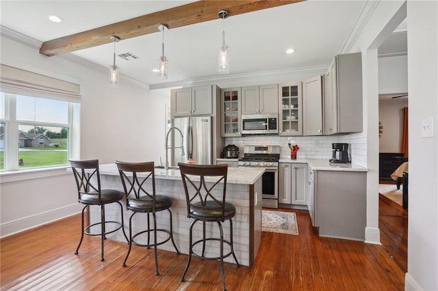 kitchen with gray cabinetry, pendant lighting, a center island with sink, beamed ceiling, and stainless steel appliances