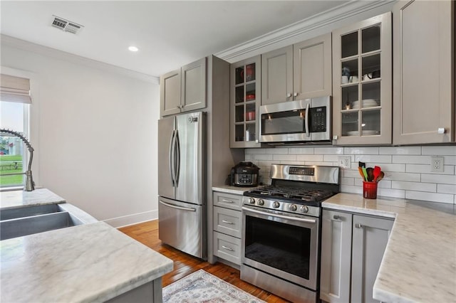 kitchen with tasteful backsplash, visible vents, glass insert cabinets, stainless steel appliances, and gray cabinetry