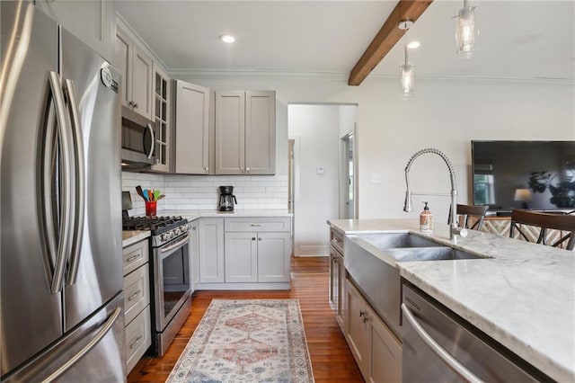 kitchen featuring decorative light fixtures, wood finished floors, a sink, appliances with stainless steel finishes, and glass insert cabinets