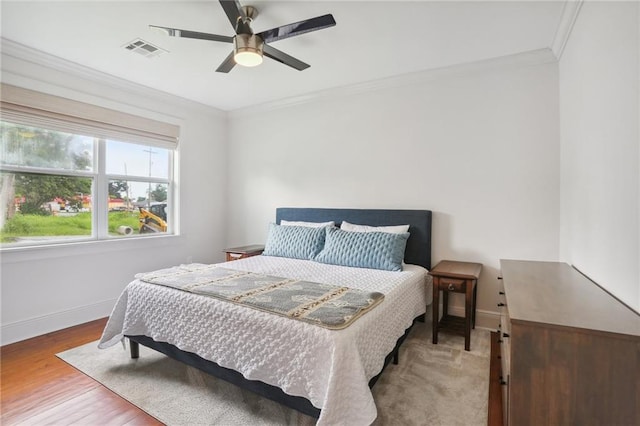 bedroom featuring baseboards, visible vents, wood finished floors, and ornamental molding