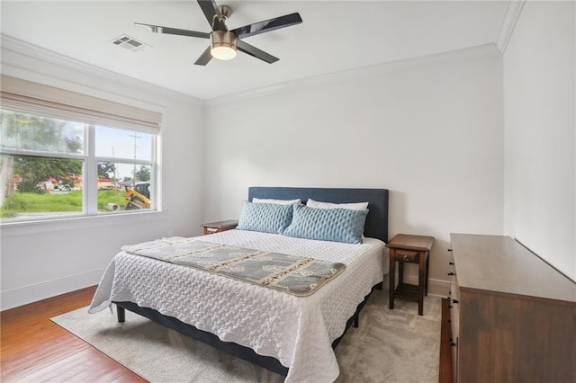 bedroom featuring ornamental molding, visible vents, baseboards, and wood finished floors