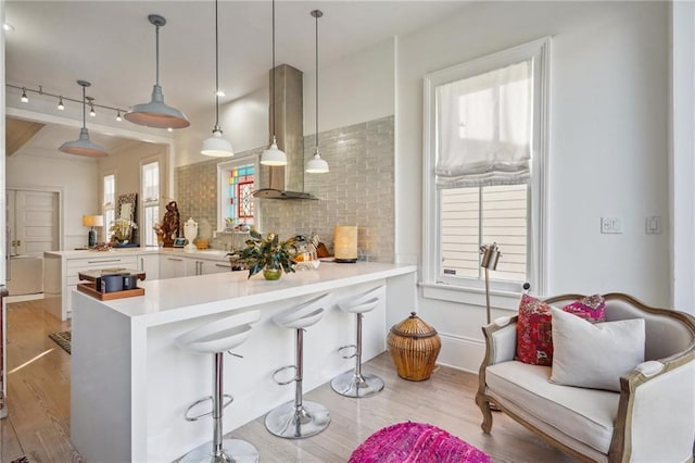 kitchen with kitchen peninsula, wall chimney range hood, pendant lighting, light hardwood / wood-style floors, and a breakfast bar area