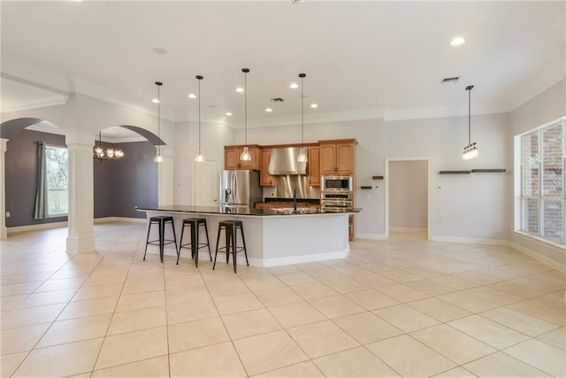 kitchen with hanging light fixtures, decorative columns, a kitchen bar, a center island with sink, and appliances with stainless steel finishes