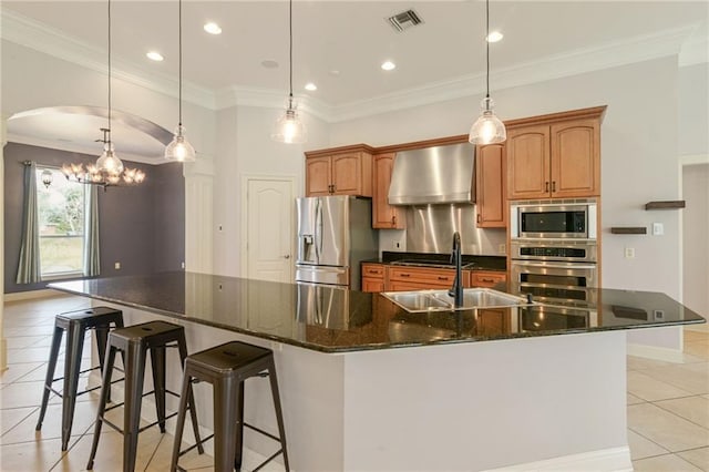 kitchen featuring appliances with stainless steel finishes, decorative light fixtures, a large island, and wall chimney range hood