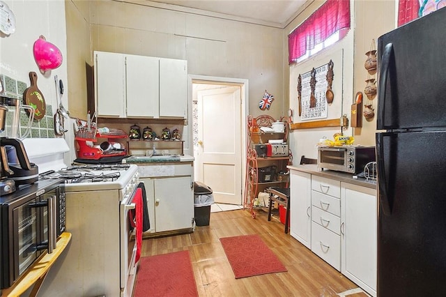 kitchen with black refrigerator, light wood-type flooring, white gas range oven, sink, and white cabinetry