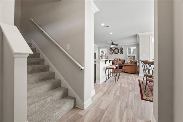 stairs with crown molding, ceiling fan, and wood-type flooring