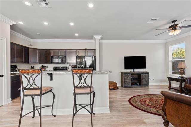 kitchen featuring a kitchen bar, light hardwood / wood-style flooring, an island with sink, light stone countertops, and black appliances