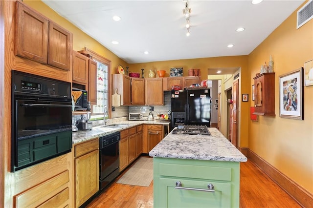 kitchen featuring tasteful backsplash, sink, a center island, black appliances, and light stone countertops