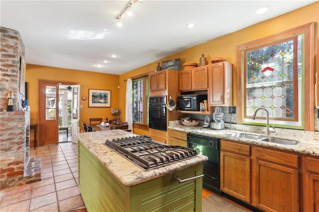 kitchen with sink, a center island, light tile patterned floors, light stone counters, and black appliances