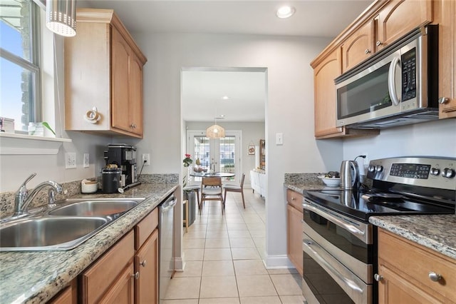 kitchen with light stone counters, stainless steel appliances, sink, light tile patterned floors, and hanging light fixtures