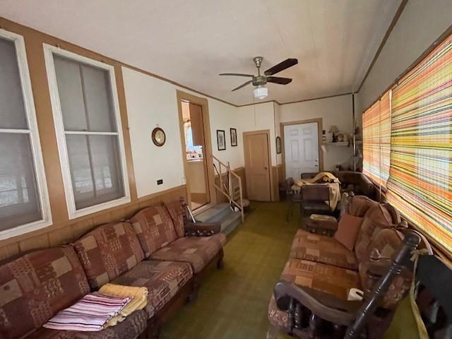 living room featuring ceiling fan, ornamental molding, and wood walls